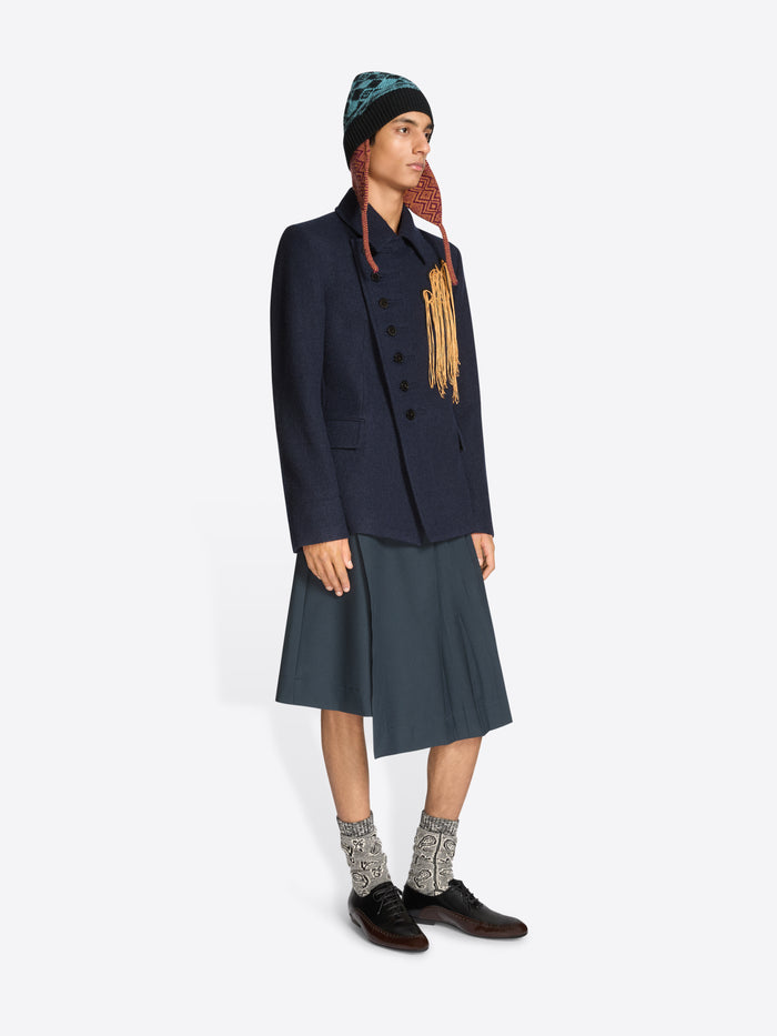 Person wearing a dark coat, skirt, patterned hat and black shoes on a white background