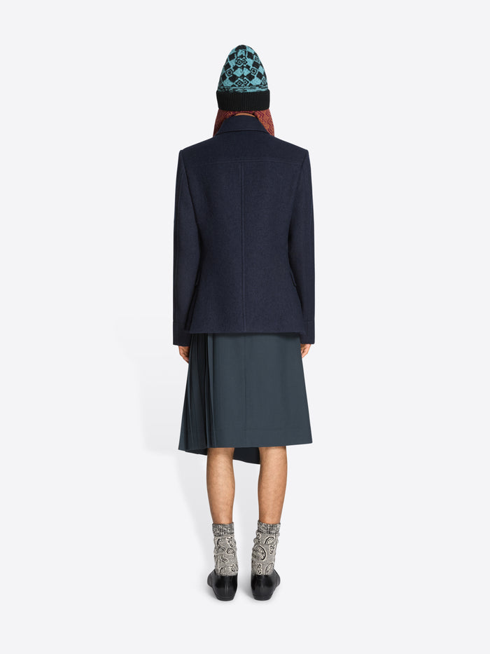 Back view of a person wearing a dark coat, skirt, patterned hat and black shoes on a white background