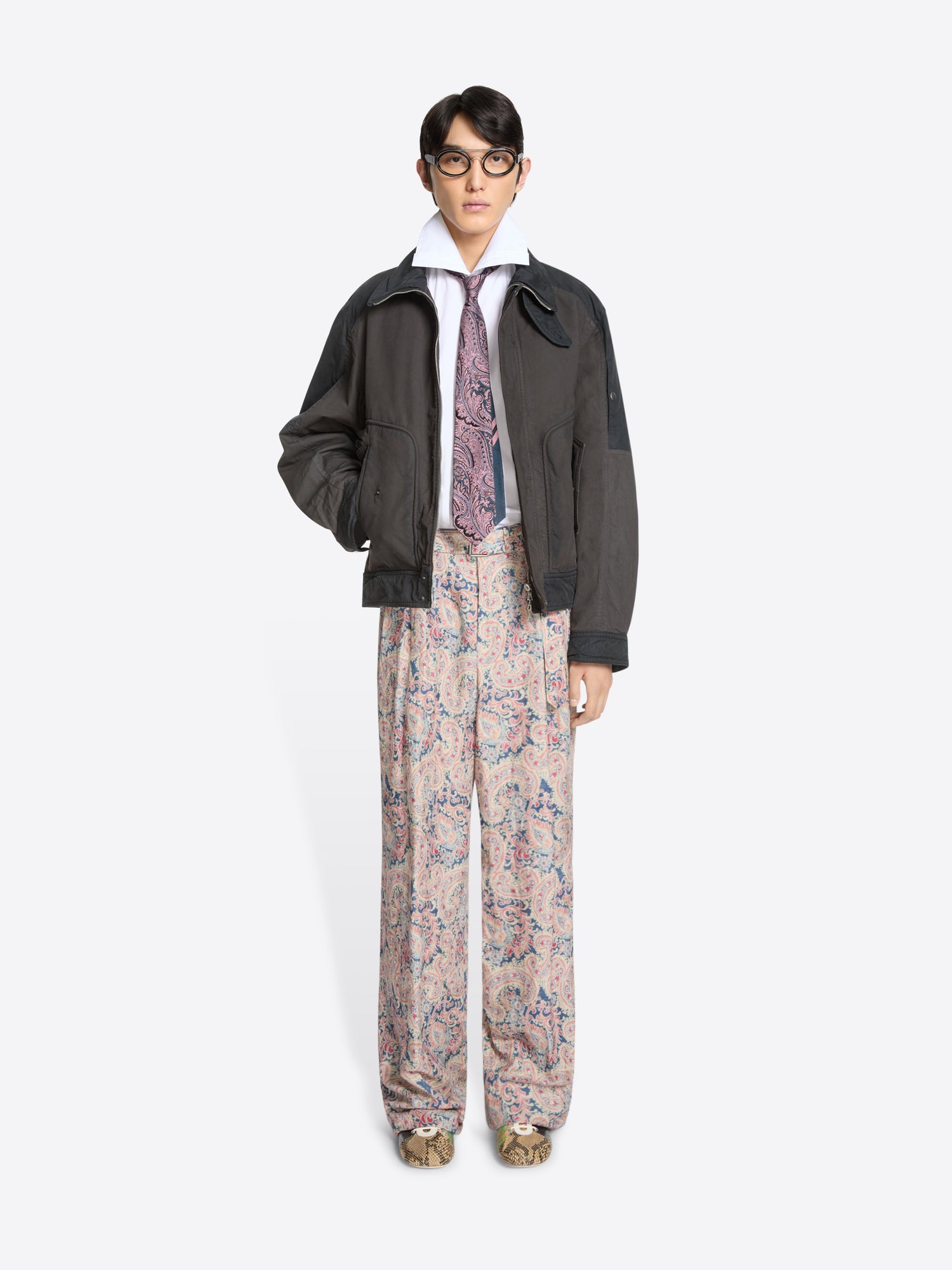 Person wearing a dark jacket, white shirt patterned tie, and floral pants on a white background