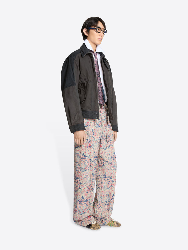 Person wearing a dark jacket, white shirt patterned tie, and floral pants on a white background