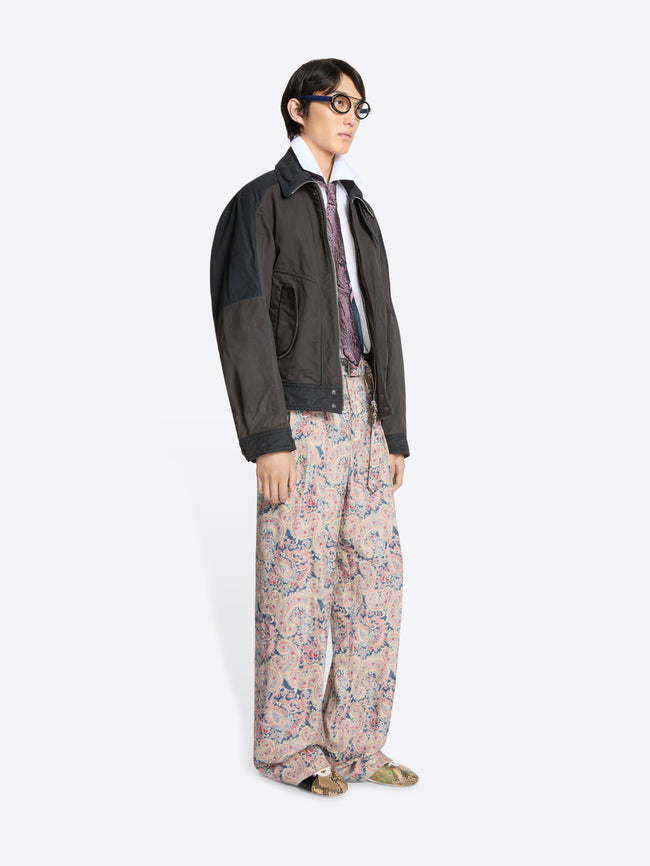 Person wearing a dark jacket, white shirt patterned tie, and floral pants on a white background
