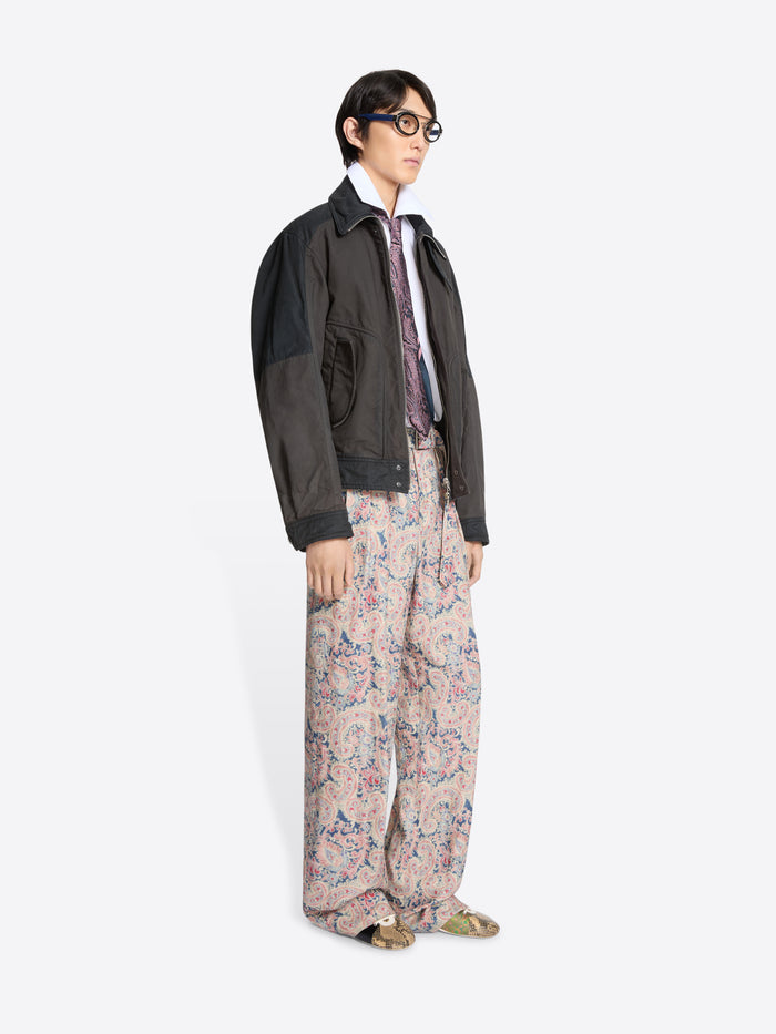 Person wearing a dark jacket, white shirt patterned tie, and floral pants on a white background