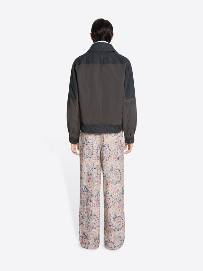 Back view of a person wearing a dark jacket, white shirt patterned tie, and floral pants on a white background