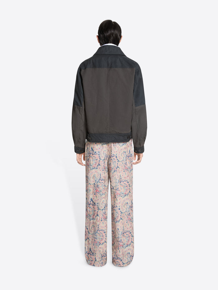 Back view of a person wearing a dark jacket, white shirt patterned tie, and floral pants on a white background