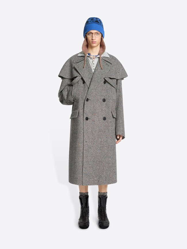 Person wearing a gray coat, blue hat, and black boots on a white background