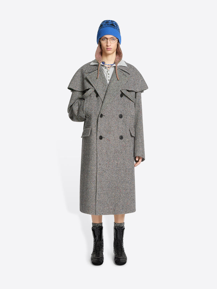 Person wearing a gray coat, blue hat, and black boots on a white background