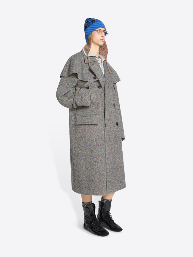 Person wearing a gray coat, blue hat, and black boots on a white background