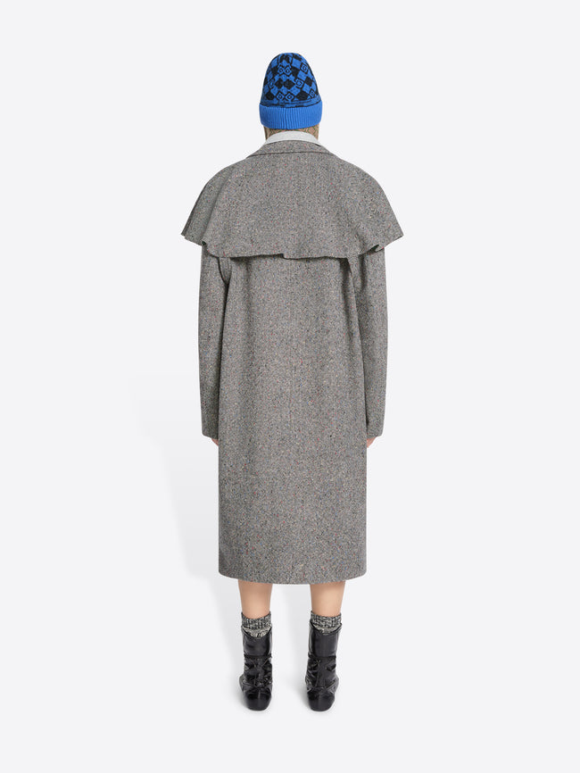 Back view of a person wearing a gray coat, blue hat, and black boots on a white background