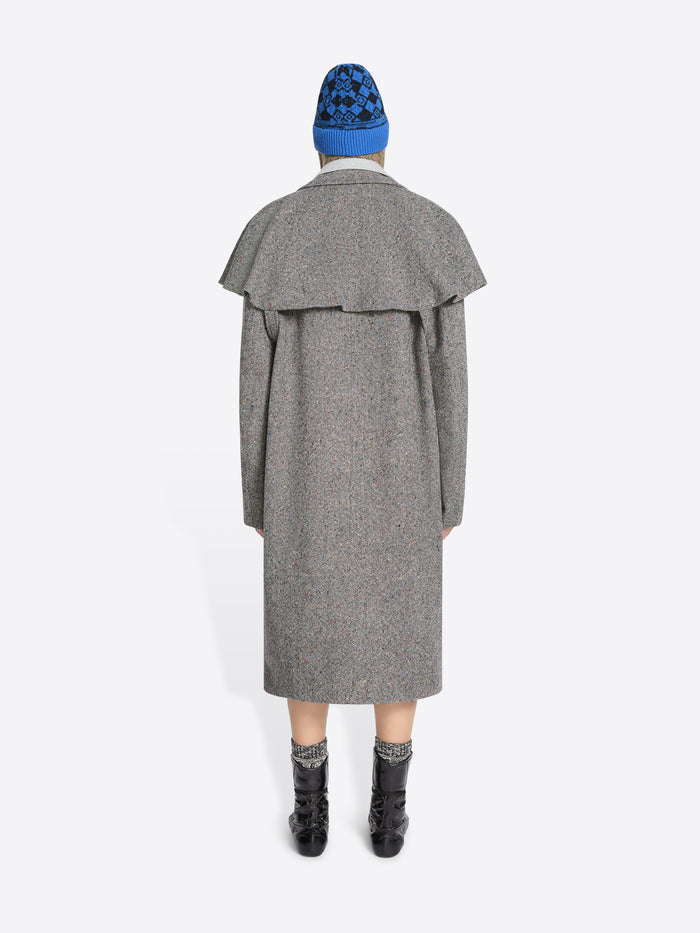 Back view of a person wearing a gray coat, blue hat, and black boots on a white background