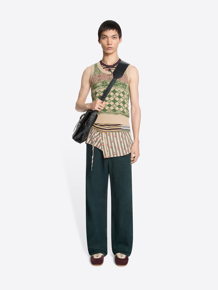 Model wearing a patterned sleeveless top,  dark pants and striped wrap belt with floral pattern with a black bag on a white background