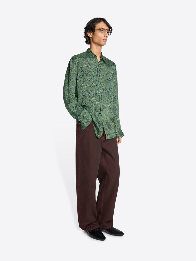 Person wearing a green long-sleeve button-up shirt and loose dark pants on a white background 