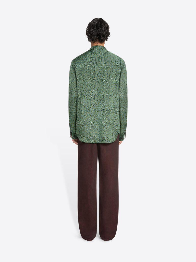 Back view of a person wearing a green long-sleeve button-up shirt and loose dark pants on a white background 