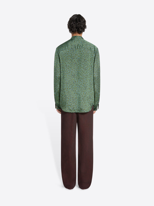 Back view of a person wearing a green long-sleeve button-up shirt and loose dark pants on a white background 