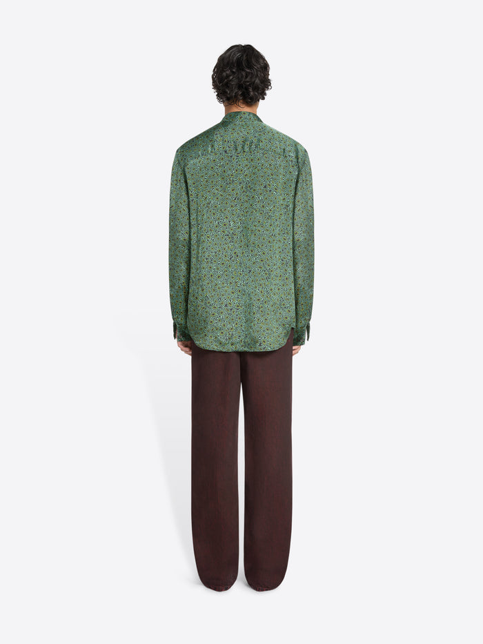 Back view of a person wearing a green long-sleeve button-up shirt and loose dark pants on a white background 