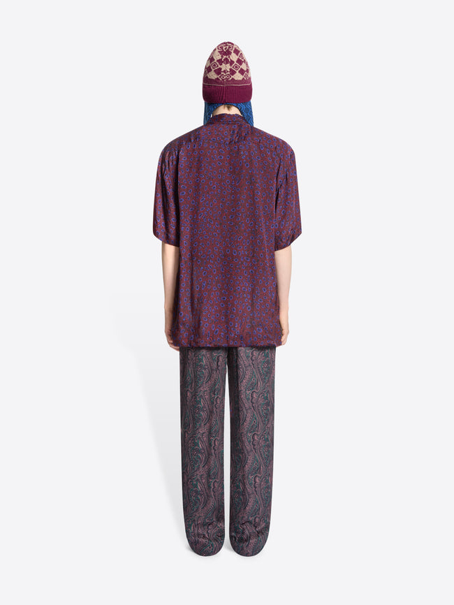 Person wearing a patterned shirt, pants and colorful hat on a white background