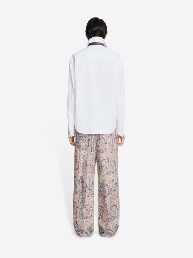 Back view of a person wearing a white shirt and patterned pants on a white background