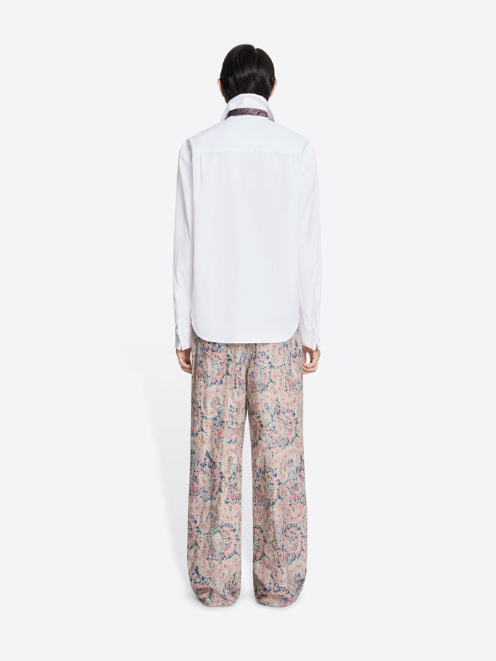 Back view of a person wearing a white shirt and patterned pants on a white background