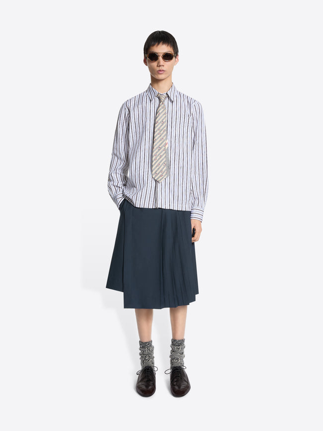 Person wearing a striped shirt, tie, and dark skirt on a white background