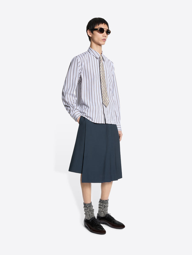 Person wearing a striped shirt, tie, and dark skirt on a white background
