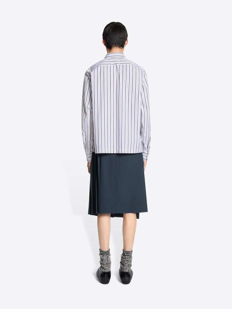 Back view of a person wearing a striped shirt and dark skirt on a white background