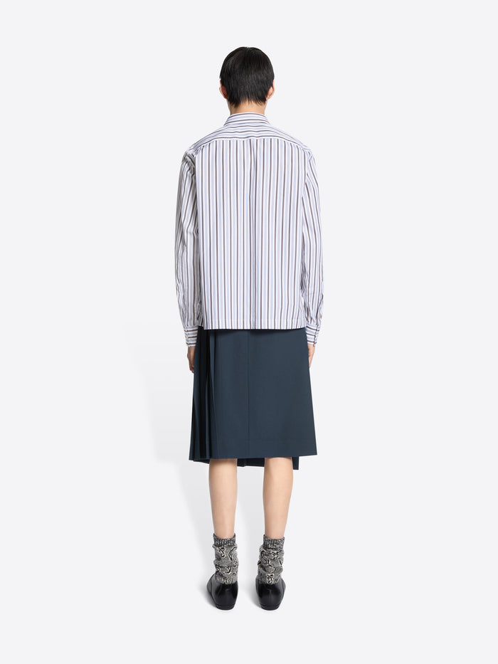 Back view of a person wearing a striped shirt and dark skirt on a white background