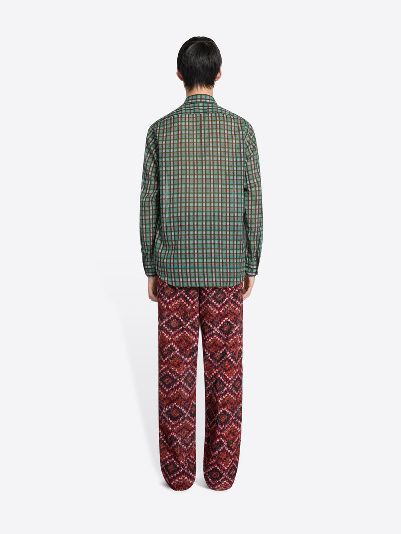 Back view of a person wearing a green checkered shirt and red patterned pants on a white background
