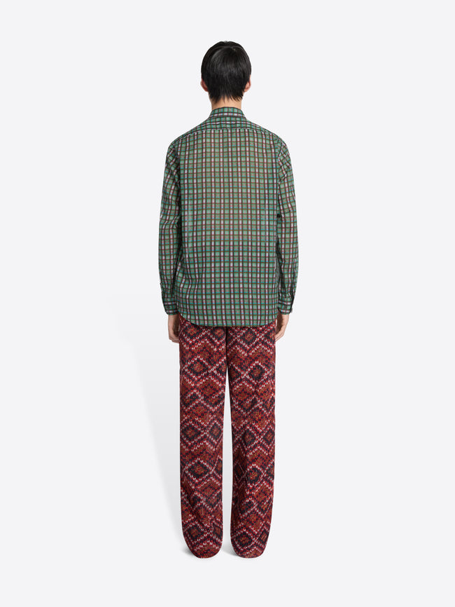Back view of a person wearing a green checkered shirt and red patterned pants on a white background