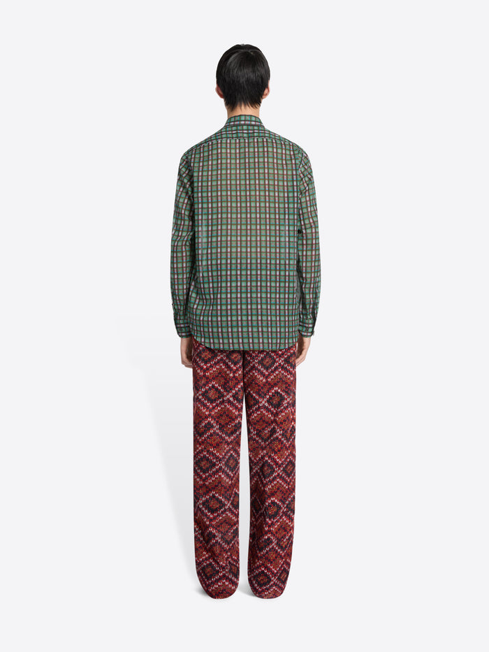 Back view of a person wearing a green checkered shirt and red patterned pants on a white background