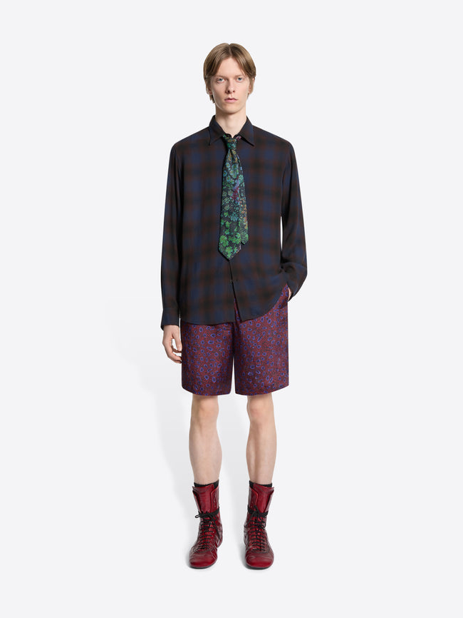 Person wearing a plaid shirt, patterned tie, purple shorts, and red boots on a white background