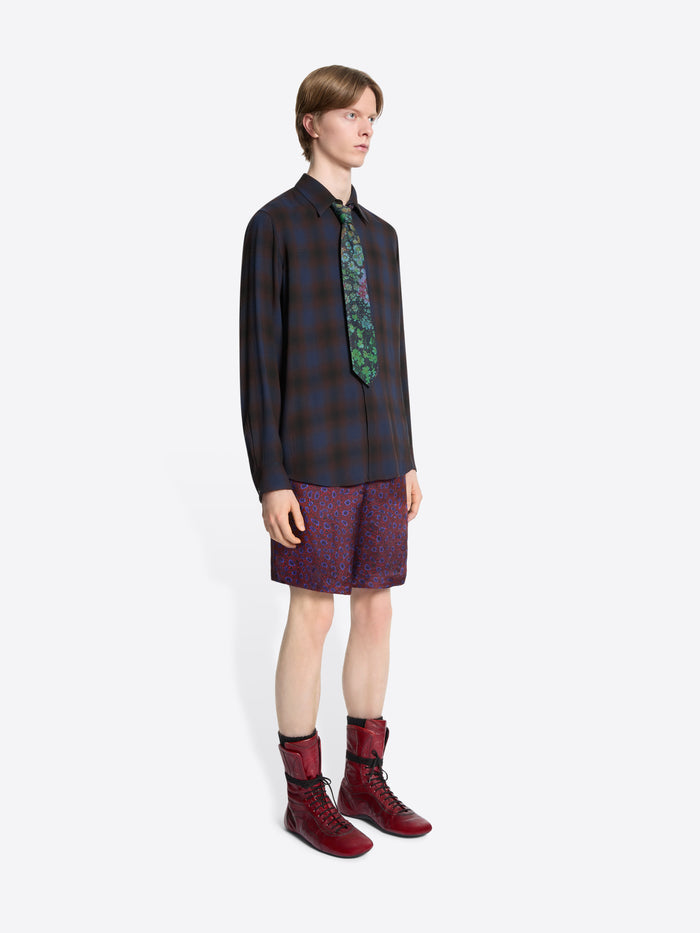 Person wearing a plaid shirt, patterned tie, purple shorts, and red boots on a white background