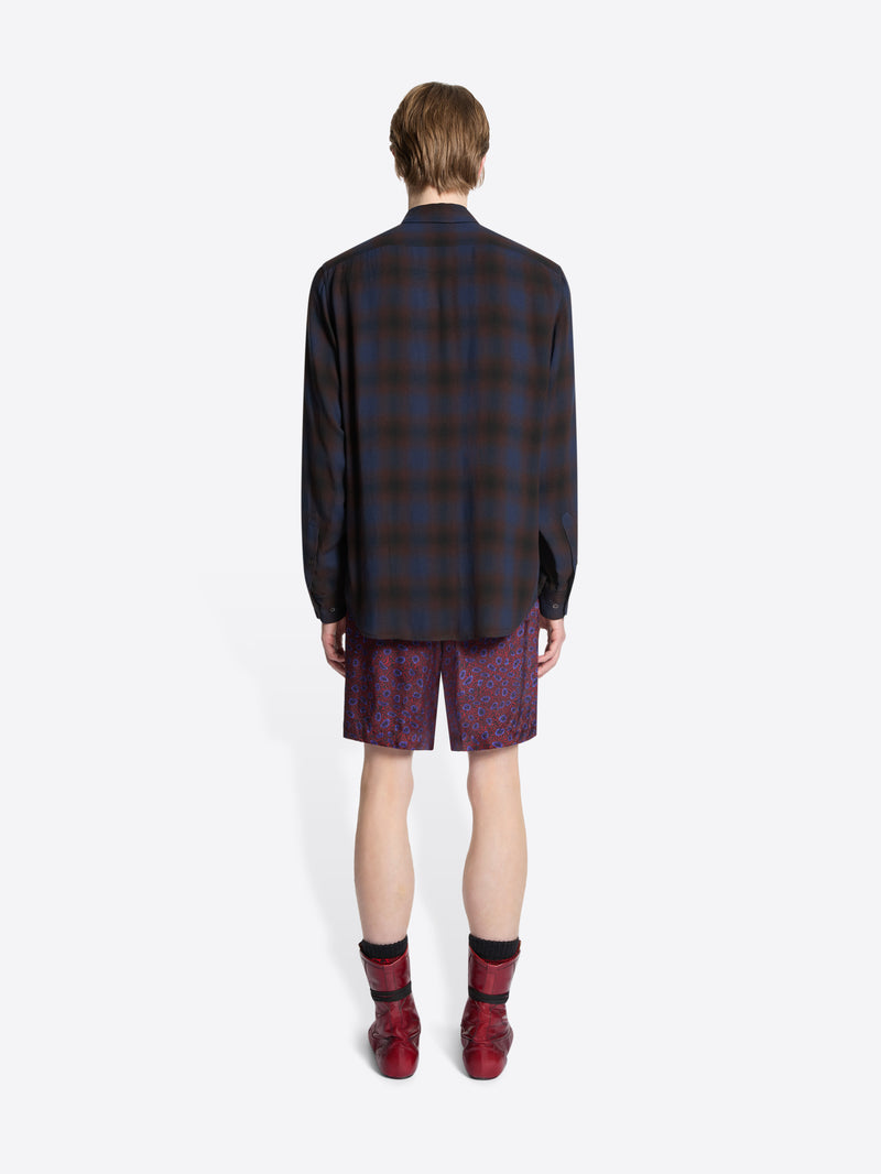 Person wearing a plaid shirt, patterned tie, purple shorts, and red boots on a white background