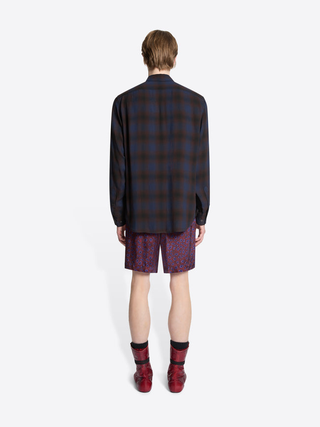 Person wearing a plaid shirt, patterned tie, purple shorts, and red boots on a white background