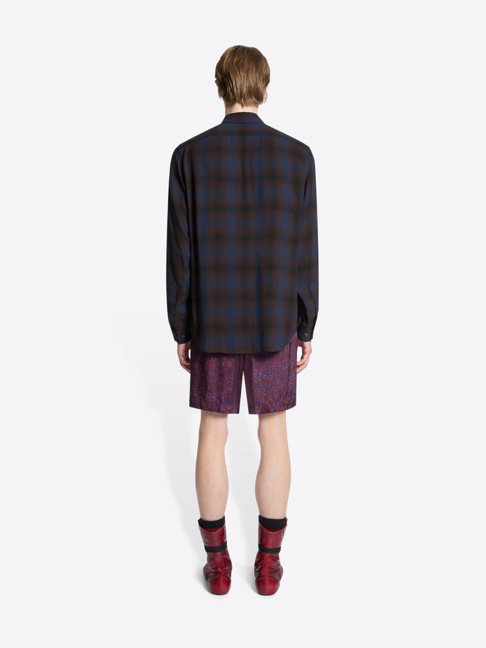 Person wearing a plaid shirt, patterned tie, purple shorts, and red boots on a white background