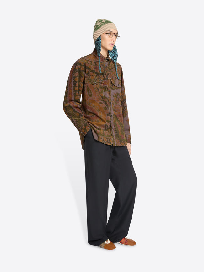 Person wearing a patterned shirt, black pants, and a hat on a white background