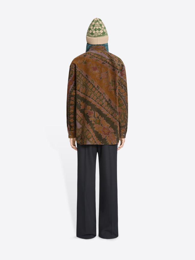 Back view of a person wearing a patterned shirt, black pants, and a hat on a white background
