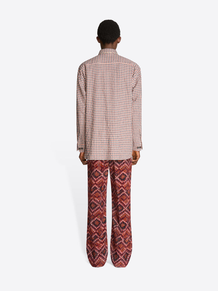 Back view of a person wearing a checkered shirt and patterned pants on a white background