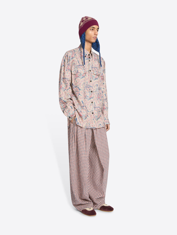 Person wearing a patterned shirt and checkered pants with a colorful hat on a white background