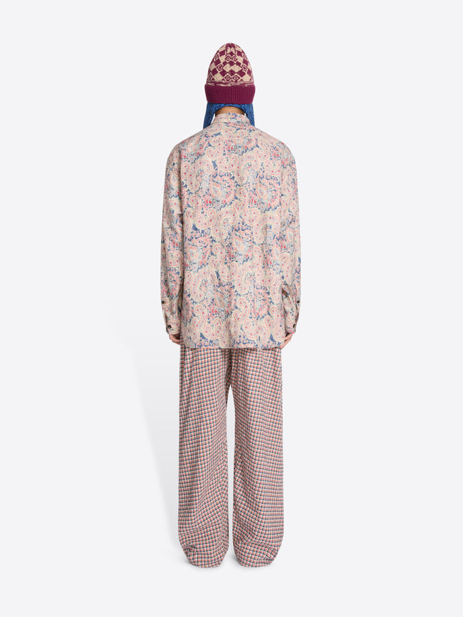 Back view of a person wearing a patterned shirt and checkered pants with a colorful hat on a white background