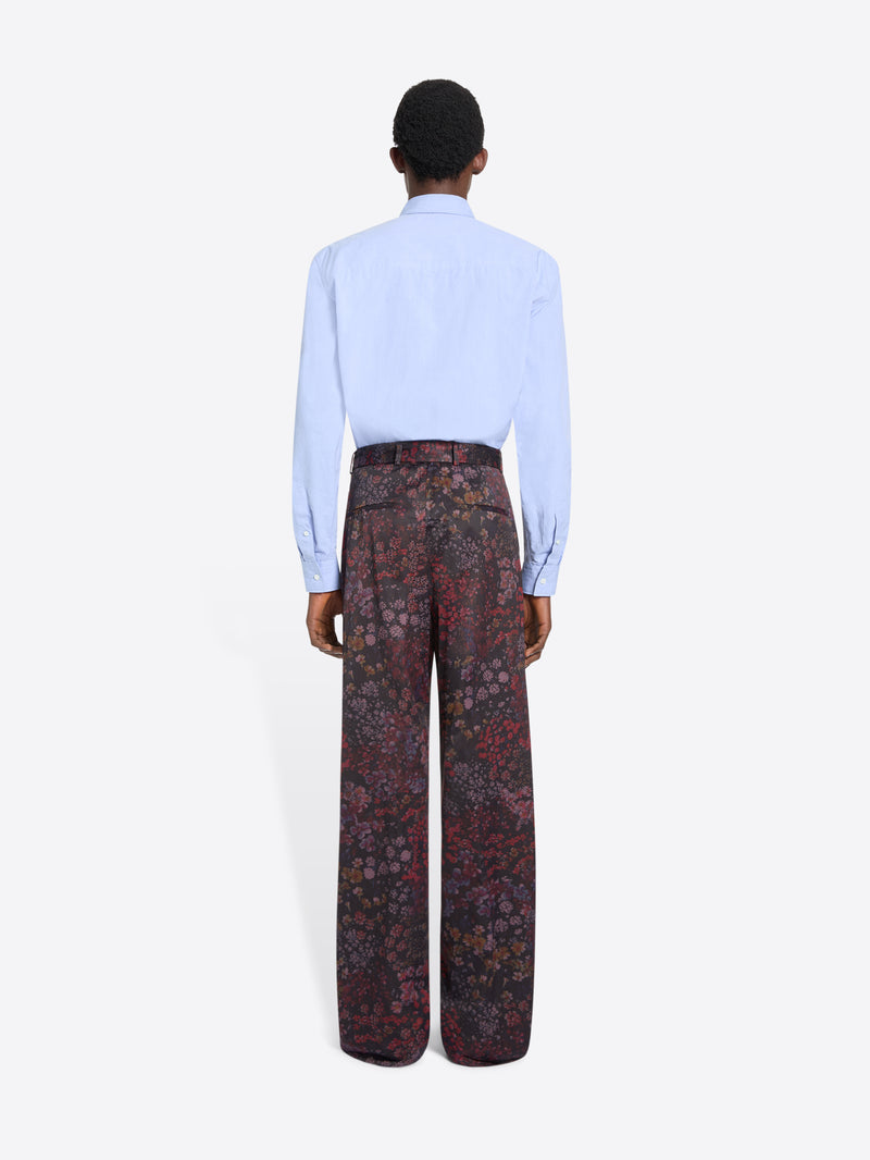 Back view of a person wearing a light blue shirt and patterned pants on a white background