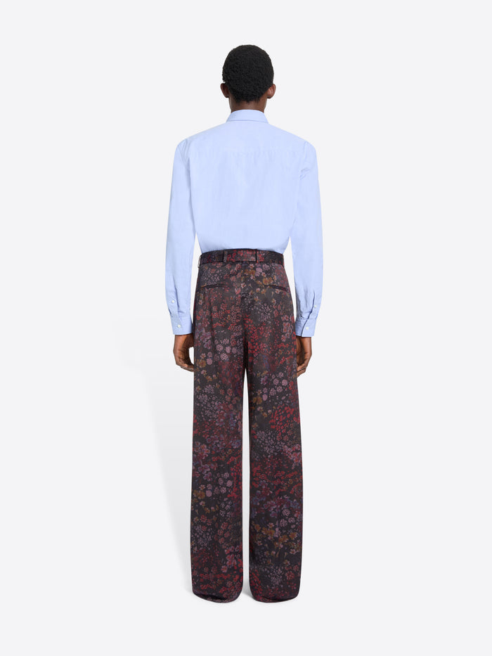 Back view of a person wearing a light blue shirt and patterned pants on a white background