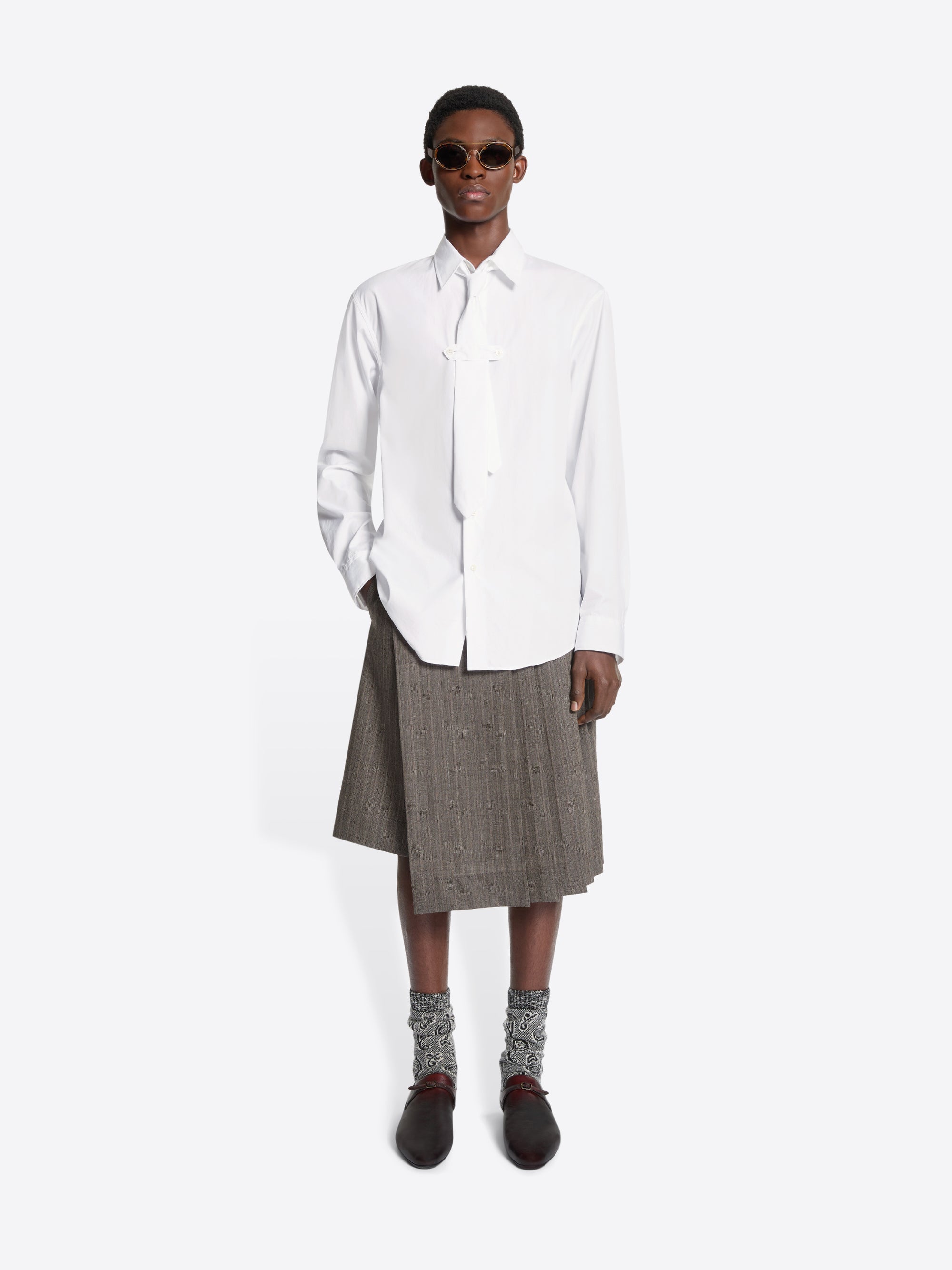 Person wearing a white shirt, gray skirt, and brown shoes on a white background