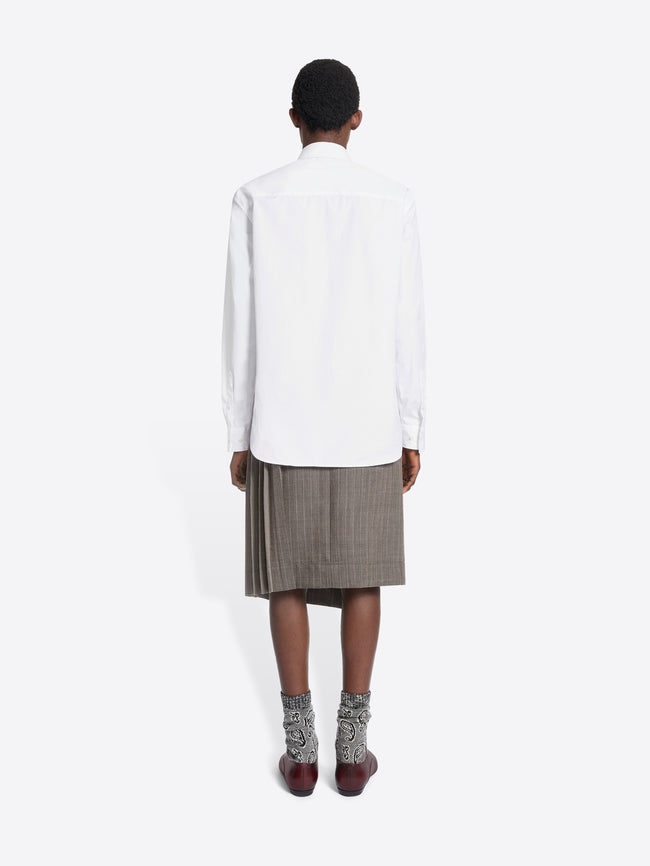 Person wearing a white shirt, gray skirt, and brown shoes on a white background