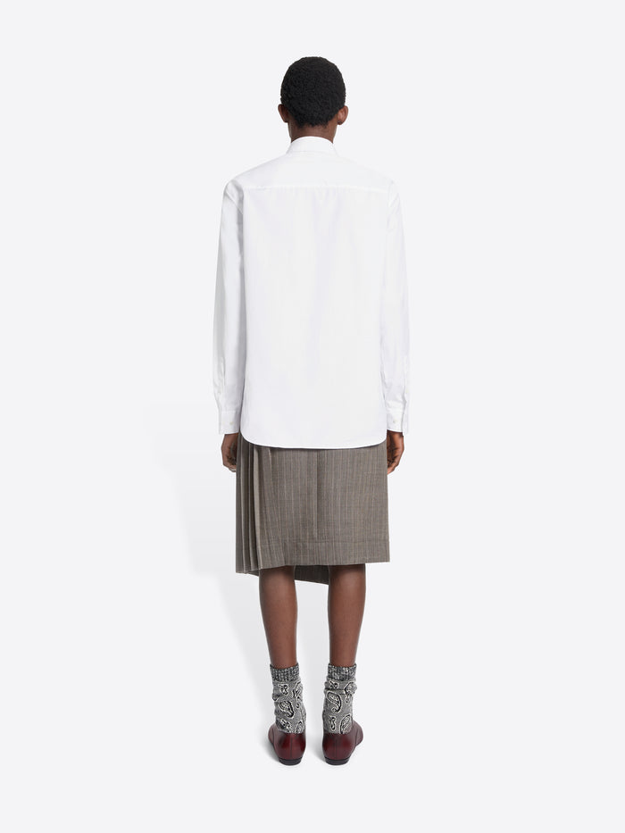 Person wearing a white shirt, gray skirt, and brown shoes on a white background
