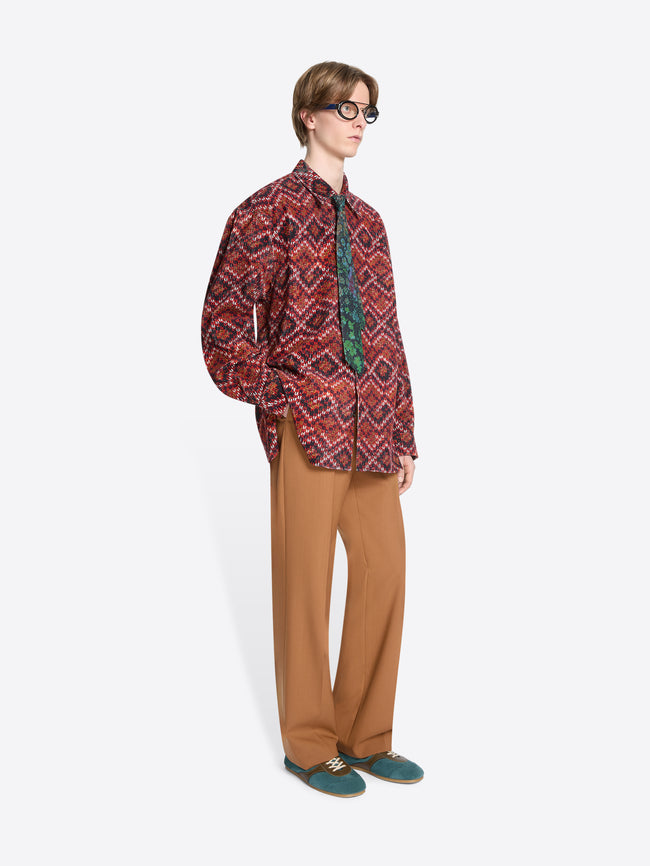 Person wearing a patterned shirt and orange pants on a white background