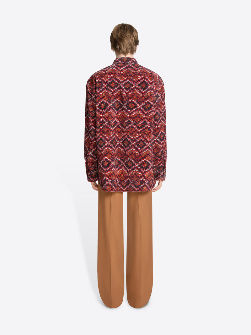 Back view of a person wearing a patterned shirt and orange pants on a white background