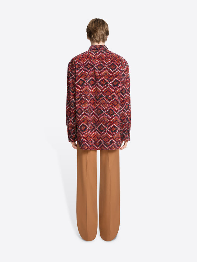 Back view of a person wearing a patterned shirt and orange pants on a white background