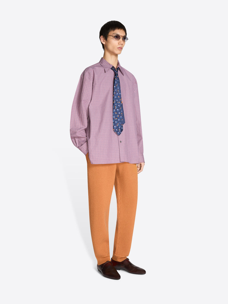 Person wearing a purple shirt, patterned tie, and orange pants on a white background