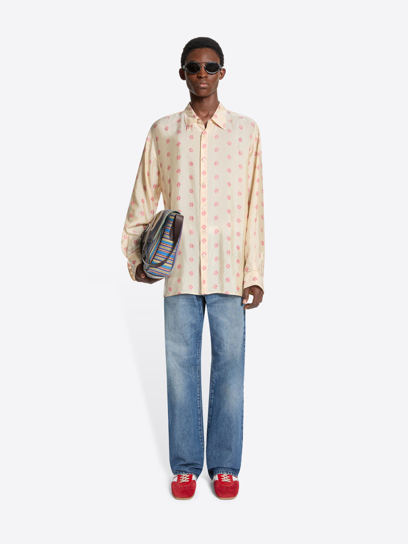 Person wearing a patterned shirt, jeans, and red shoes holding a striped bag on a white background