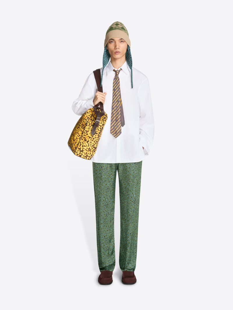 Person wearing a white shirt, green patterned pants, and holding a patterned bag on a white background