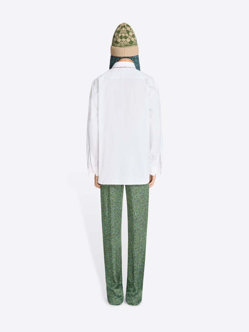 Back view of a person wearing a white shirt and green pants with a patterned hat on a white background